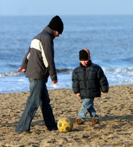 Padre e hijo jugando al futbol en la playa